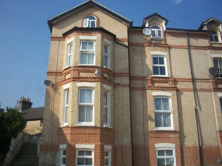 Victorian apartment building in yellow brick with red brick banding, bay windows, white sash windows and arched dormers under a clear blue sky