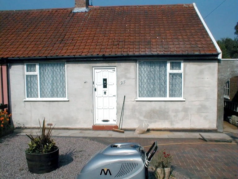 Single-storey rendered bungalow with a red tiled roof and white front door, with a silver cleaning machine parked on the driveway in the foreground
