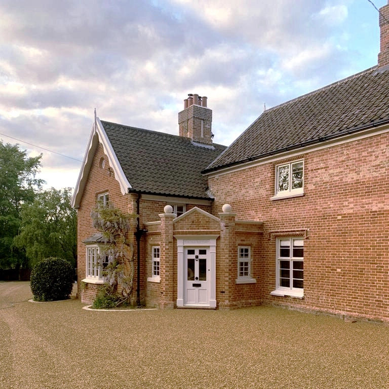 Restored red brick country house with a tiled roof, white-framed windows, a pedimented porch and a gravel driveway in the foreground