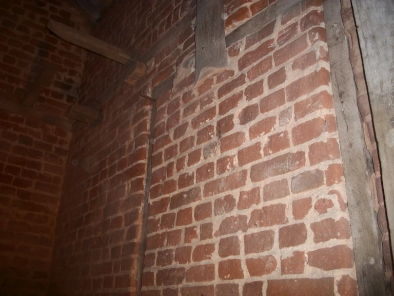 Close-up of period red brickwork with pale lime mortar joints, set between old timber beams inside a building