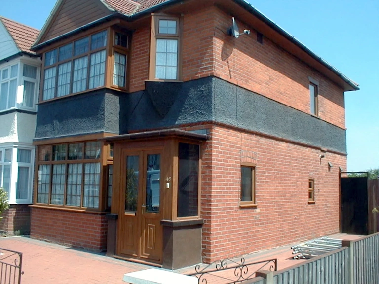 Red brick house with a dark rendered band across the middle, timber-framed windows and a porch, photographed in bright sunshine